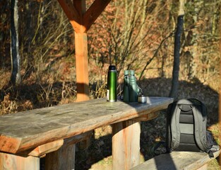 Tourist bench relaxing in the woods on the table with a thermos for coffee, binoculars and a backpack