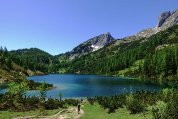 Fototapeta na wymiar trail with hikers to a blue mountain lake in the summer