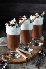 A row of chocolate mousse dessert parfaits on a wooden board against a dark background.