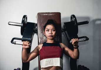 A sporty asian girl does some machine shoulder presses. Working out delts at the gym.