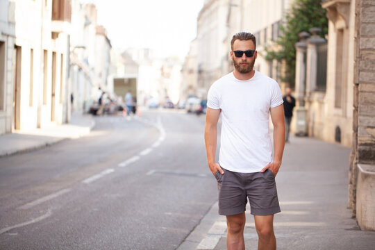 Hipster handsome male model with beard wearing white blank t-shirt and a baseball cap with space for your logo or design in casual urban style