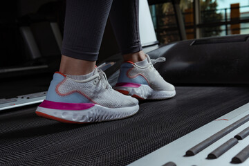 Young beautiful woman on the treadmill in the gym. Close-up shoes appear.