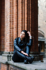 Portrait of beautiful young brunette woman in stylish black leather jacket, smiling on urban back