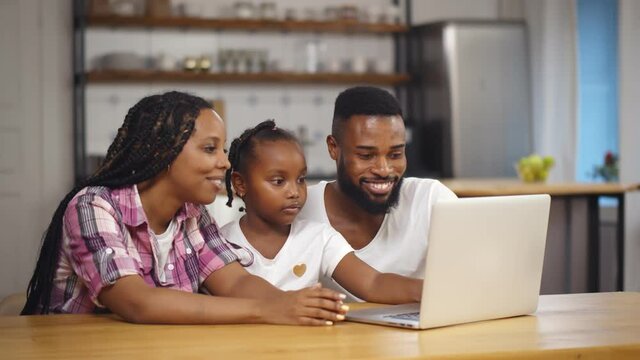 Happy african family with kid sit at table using laptop and giving high five