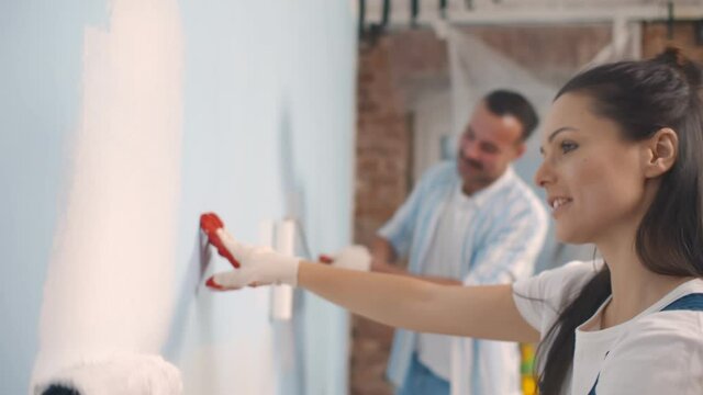 Young happy couple repairing and painting wall at home