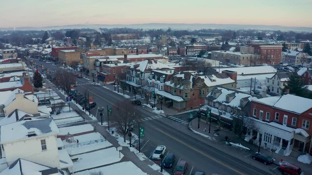 Aerial establishing shot of Main Street, Small Town America, storefronts and colonial homes in United States historic town during winter snow.
