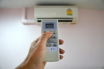 The hand is holding the air conditioner remote control and pressing the button to adjust the temperature to 25 degrees Celsius