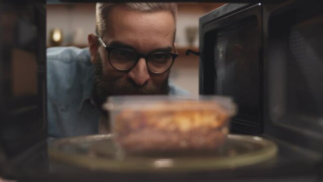 Man putting leftover dinner into microwave oven to cook