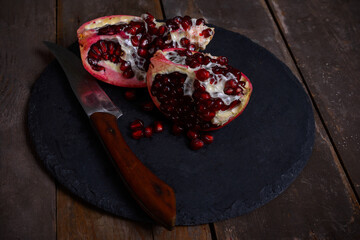 Pomegranate cut in half with a knife on a wooden background.
