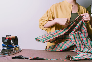 Fototapeta na wymiar Female ironing plaid fabric in sewing workshop