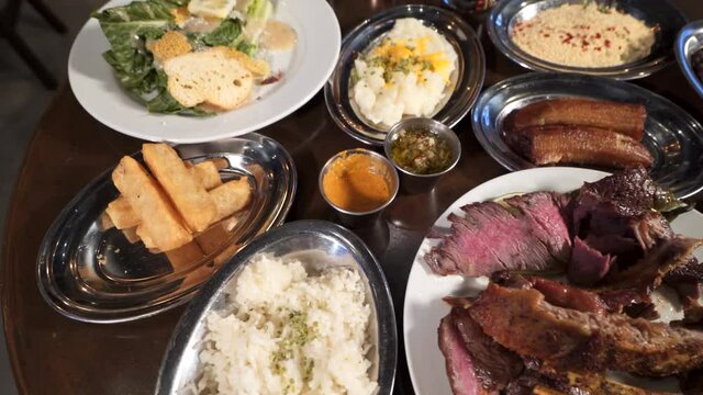 Table filled with various offerings at a Brazilian steakhouse, close up slider slow motion 4K