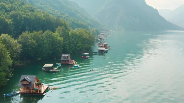Aerial, Wooden houses floating on Perucac lake surrounded by mountains on the foggy day.