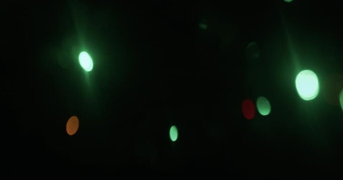 Medium tracking shot of lights on a Christmas tree filmed with lens adapted to create oval bokeh and distort image on the edges. The camera tracks right as some of the lights slowly fade in and out.