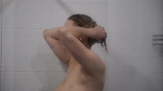 Woman washing hair behind glass of shower stall