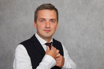 An attractive man holds a tie and looks at the camera. A handsome man in white shirt tying tie. A man in a white shirt ties his tie.