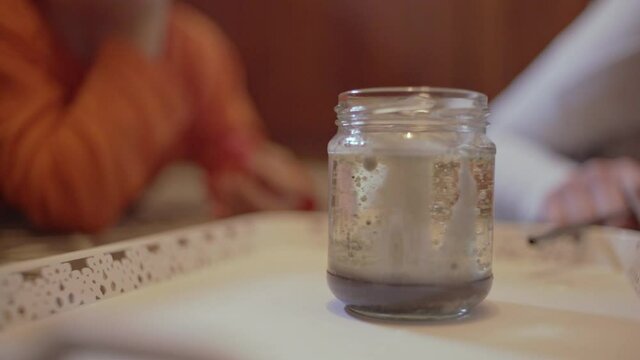 Close up on a vase with sodium tetra borate, stirred and producing bubbles, mother and child doing an experiment at home