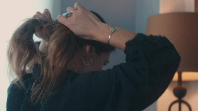 Young woman ties curly blonde hair into ponytail with scrunchie, Closeup