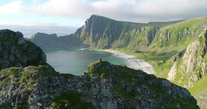 Aerial rear view of hiker on mountain ridge looking at arctic white sand beach