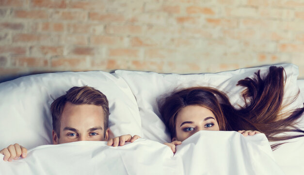 Young couple peeping from bedsheet on the bed at bedroom. Love, relationship, dating, happy people, bedtime concept picture.