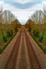 Fototapeta na wymiar Symmetrical train tracks shot taken with view down and into the distance. Trees line both sides of the railway lines