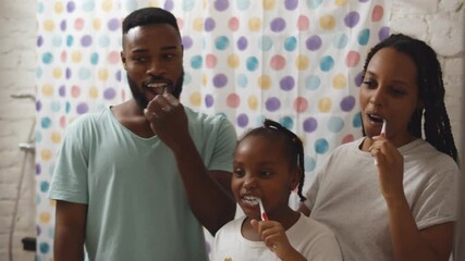 Happy african family brushing teeth together in bathroom standing in front of mirror