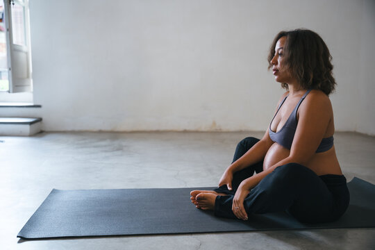 Young pregnant woman sitting on the mat making meditation and prenatal exercises at a yoga class - Concept of life and maternity