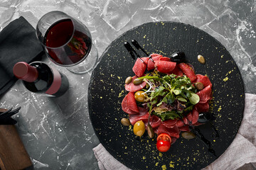 Beef carpaccio with arugula on a black plate, traditional Italian cuisine. Dark key, copy space,