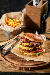 The concept of American fast food. A juicy American burger with two beef patties and a dark beer on a glass table onwooden background. Copy space