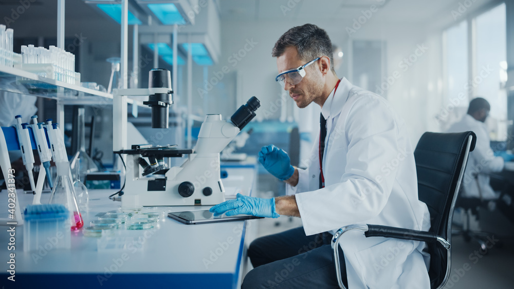 Wall mural medical development laboratory: caucasian male scientist using microscope amd enters data into digit