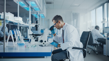 Medical Development Laboratory: Caucasian Male Scientist Looking Under Microscope, Analyzing Petri Dish Sample. Professionals Working in Advanced Scientific Lab doing Medicine, Biotechnology Research