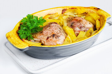 Chicken baked with potatoes and spices, in a baking dish, a bunch of greens on top. White background, selective focus