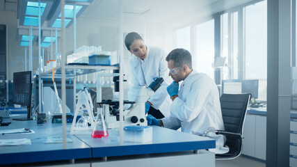 Naklejka na ściany i meble Modern Medical Research Laboratory: Portrait of Two Scientists Working, Using Microscope, Analyzing Samples, Talking. Advanced Scientific Pharmaceutical Lab for Medicine, Biotechnology Development