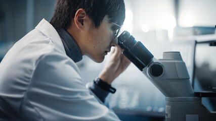 Medical Development Laboratory: Portrait of East Asian Scientist Looking Under Microscope, Analyzes Petri Dish Sample. Pharmaceutical Lab doing Medicine, Biotechnology, Microbiology, Drugs Research.