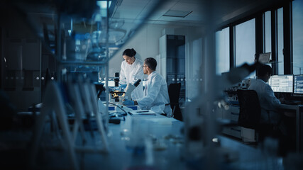 Modern Medical Research Laboratory: Two Scientists Working, Using Digital Tablet, Analyzing Test,...