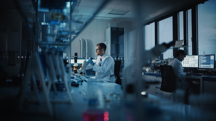 Medical Science Laboratory with Diverse Multi-Ethnic Team of Microbiology Scientists Developing Drugs, Medicine, Doing Biotechnology Research. Working on Computers, Analyzing Samples. Evening Work