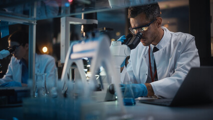 Modern Medical Research Laboratory: Male and Female Scientists Work on Laptop, Do Data Analysis,...