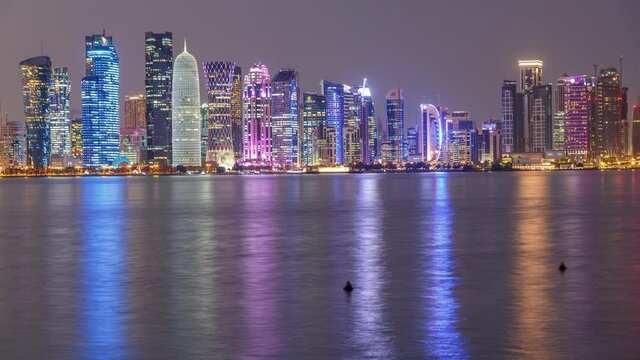 Doha downtown skyline day to night transition timelapse, Qatar, Middle East. Illuminated skyscrapers on a West Bay reflected in a water of Gulf. View from MIA park