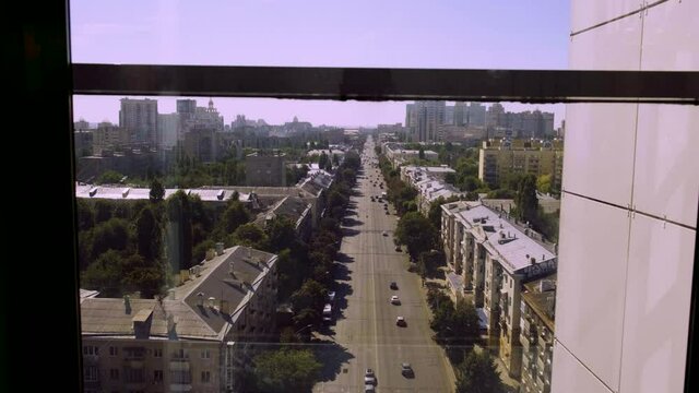A transparent glass elevator with a view of the city descends from the top floor in a skyscraper