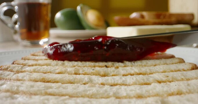 Knife spreading berry jam on piece of toast. Preparation of sweet yummy sandwich - food and drink close up 4k footage