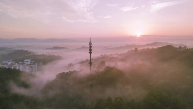4K UHD Cinematic hyperlapse Aerial footage circle view of 5G Communication tower during morning sunrise with clouds, mists and fog