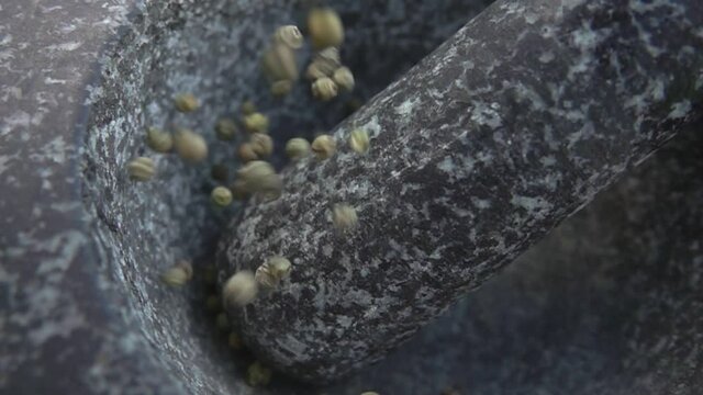 Spicy grey peppercorns are falling into the grey stone mortar in slow motion