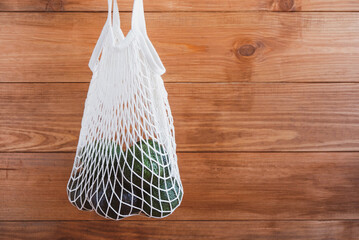 Reusable eco-friendly cotton mesh bag with avocado on wooden rustic background. Copy space. Zero waste, no plastic, sustainability. Bring your own shopping bag. Farmers market.