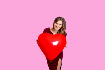 Fototapeta na wymiar A cute smiling girl on a pink background looks at the camera and holds a big red heart. The concept of the holiday is Valentine's Day, March 8, International Women's Day. Banner. Place for text
