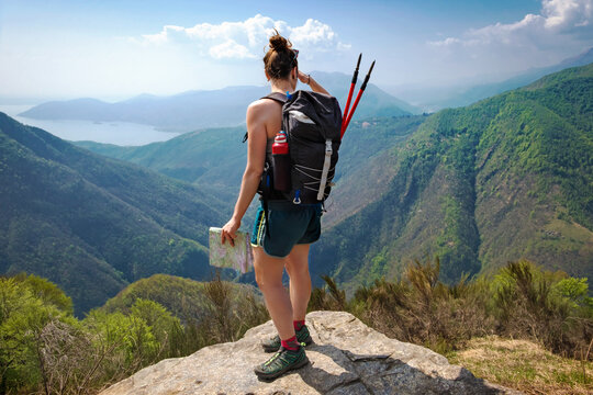 Girl hiker with backpack, trekking poles and map looking at the stunning and wild landscape of the Val grande National park from a Panoramic pointOn the background the lake Maggiore, Piedmont,Italy. 