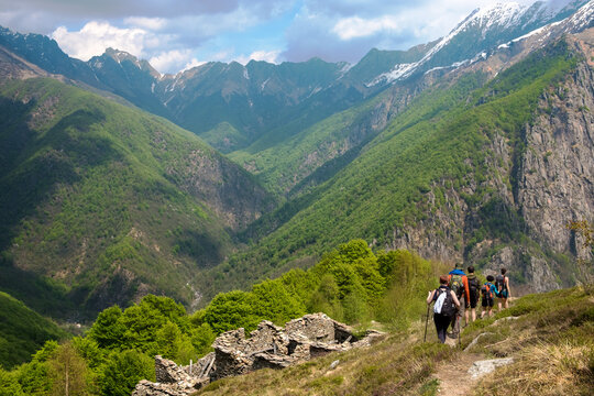 Group of hikers walks on the mountain path passing by the ruins of a hut in asunny day. the Val Grande National Park,  Europe, Piedmont Italy.