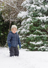 Happy child playing in the snow outdoor in winter day. Cute little toddler with warm clothes having fun in park or backyard, winter activities for kids