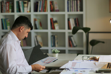 Young businessman in eyeglasses working on computer at homeoffice. Employee in eyeglasses holding paper documents,  young businessman analyzing and working with documents.