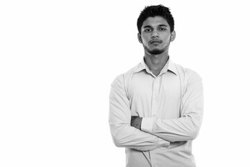 Studio shot of young handsome Indian man with arms crossed