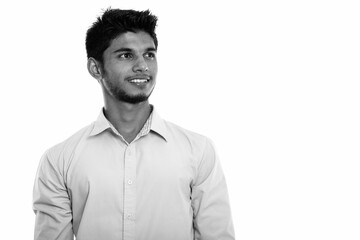 Studio shot of young happy Indian man smiling and thinking while looking up