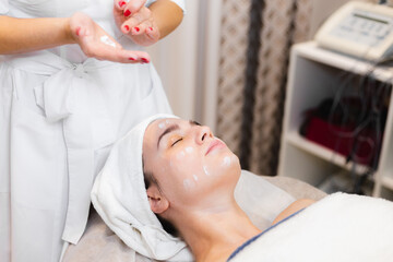Obraz na płótnie Canvas Beautician in a spa beauty salon applies cream to a client's face, a girl lies on a cosmetology table